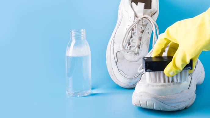 Weiße Sneaker reinigen Hand mit gelbem Handschuh reinigt mit einer Bürste weiße Snekaer